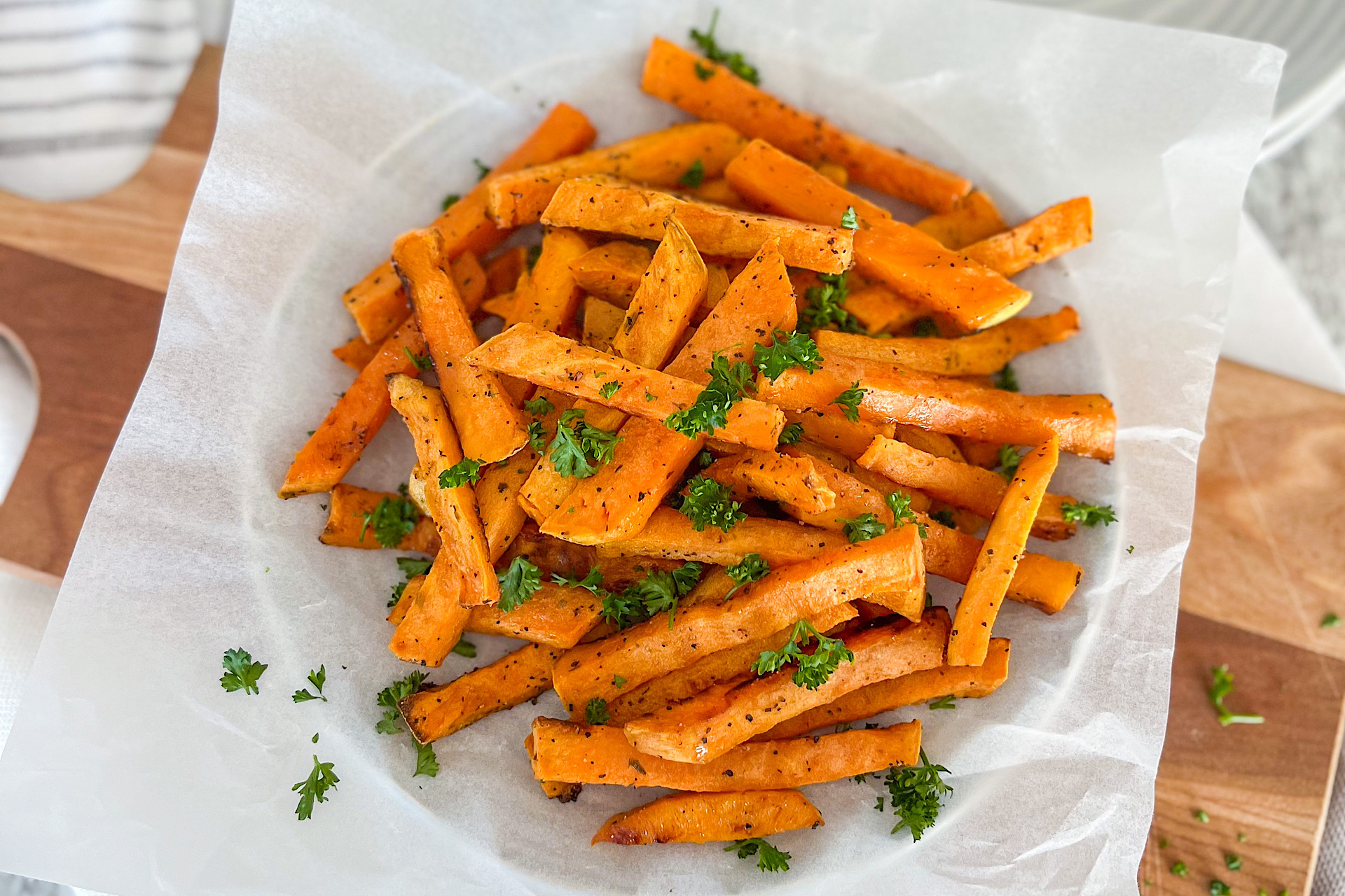 Baked sweet potato fries sprinkled with fresh green parsley and displayed on white parchment paper
