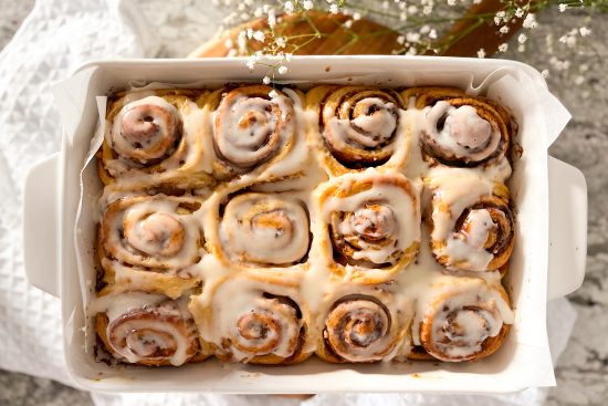 Baked, glazed with cream cheese cinnamon rolls in white baking dish,