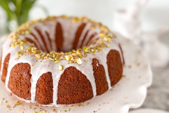 Baked orange Bundt Cake displayed on white porcelain cake stand.