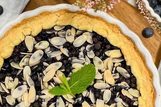 Baked Blueberry tart in white pie dish, displayed on wood board surface.