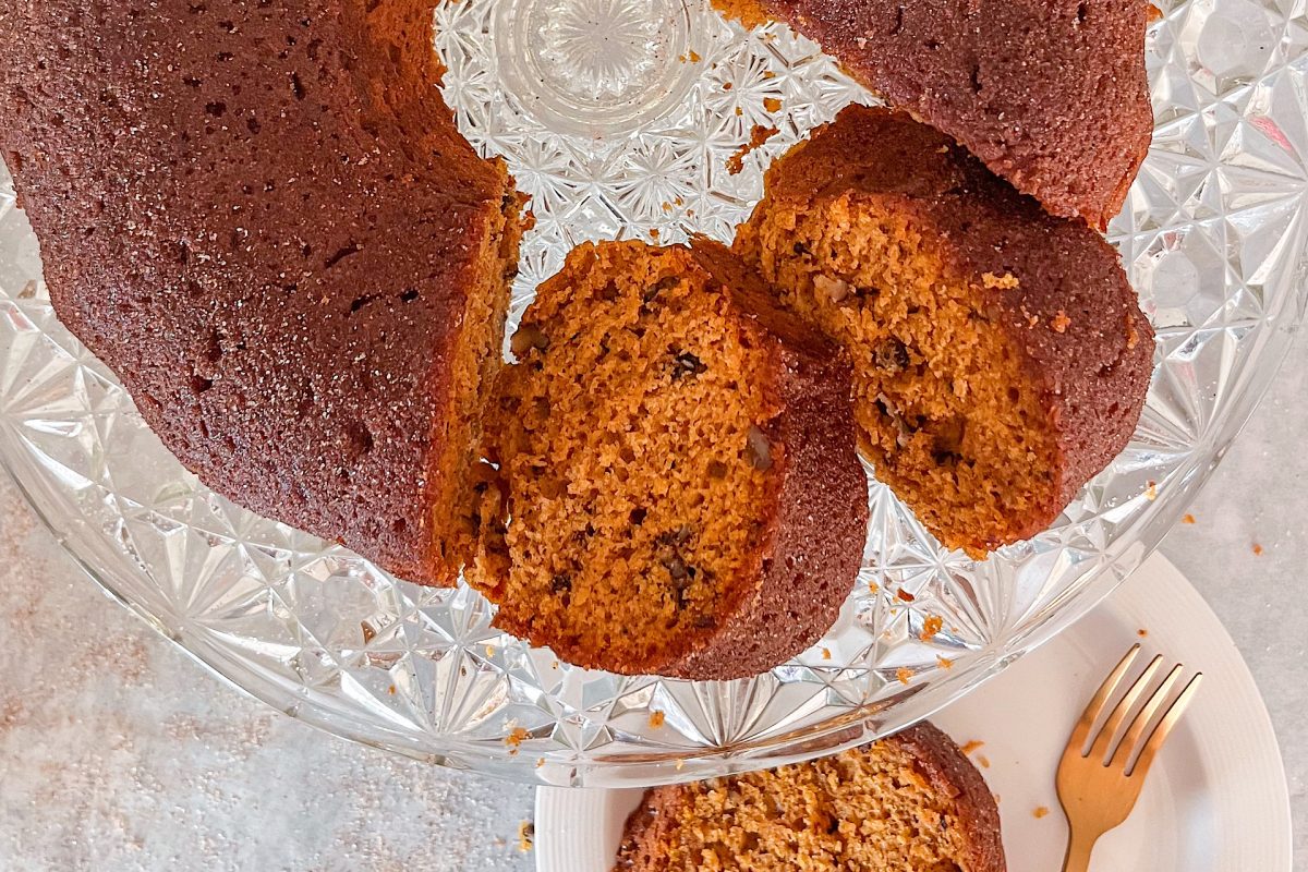 Pumpkin cake placed on glass cake stand. The 2 pieces of the cake are cut and displayed laying down.
