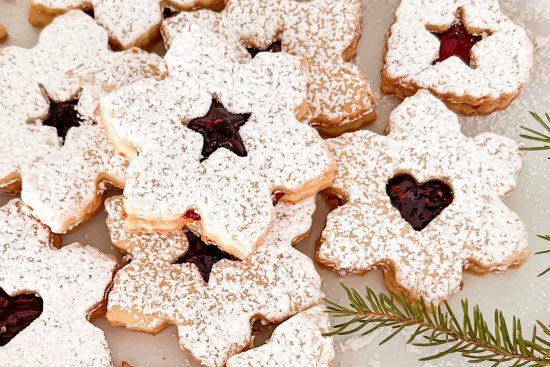 Snowflake Raspberry Coconut Linzer cookies dusted with powdered sugar, with a star shape cutout in the center of cookie