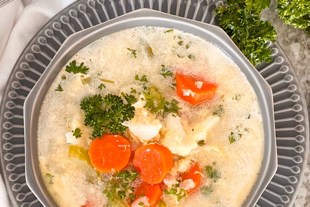 Cauliflower soup, with carrots, celery, fresh parsley in grey soup bowl