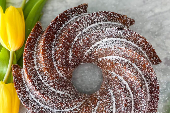 Baked Orange Chocolate Bundt Cake displayed on grey surface and two yellow tulips beside.