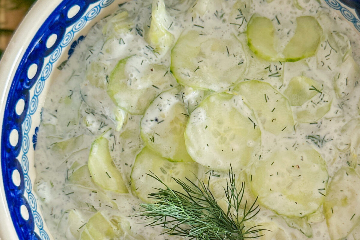 Polish cucumber salad Mizeria place in white porcelain serving dish. In the middle of the salad is placed small piece of fresh dill.