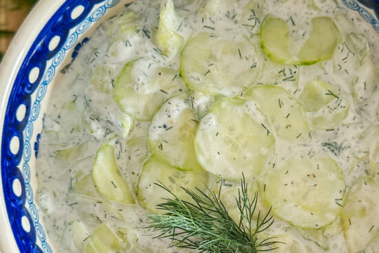 Polish cucumber salad Mizeria place in white porcelain serving dish. In the middle of the salad is placed small piece of fresh dill.