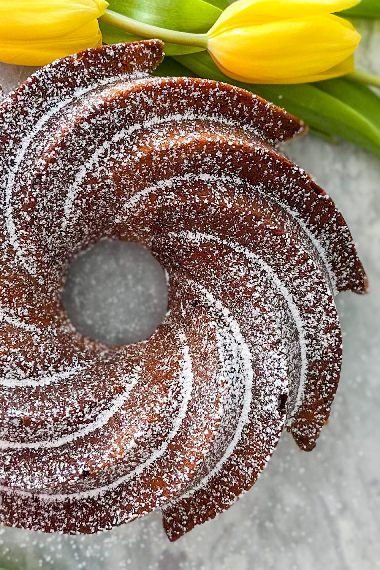 Baked Orange Chocolate Bundt Cake displayed on grey surface and two yellow tulips beside.